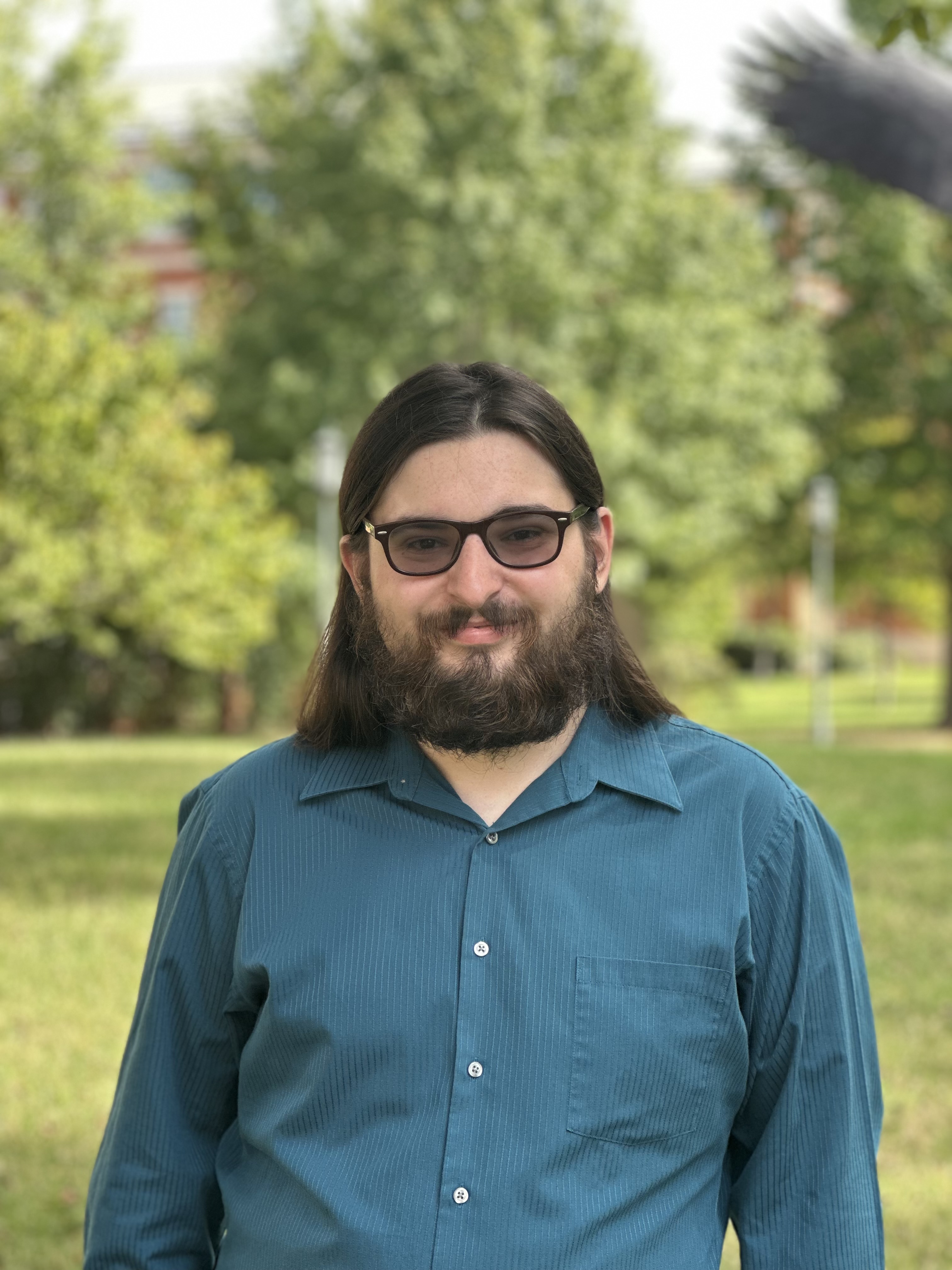 Headshot of Justin Smith, he is smiling. Trees are in the background.