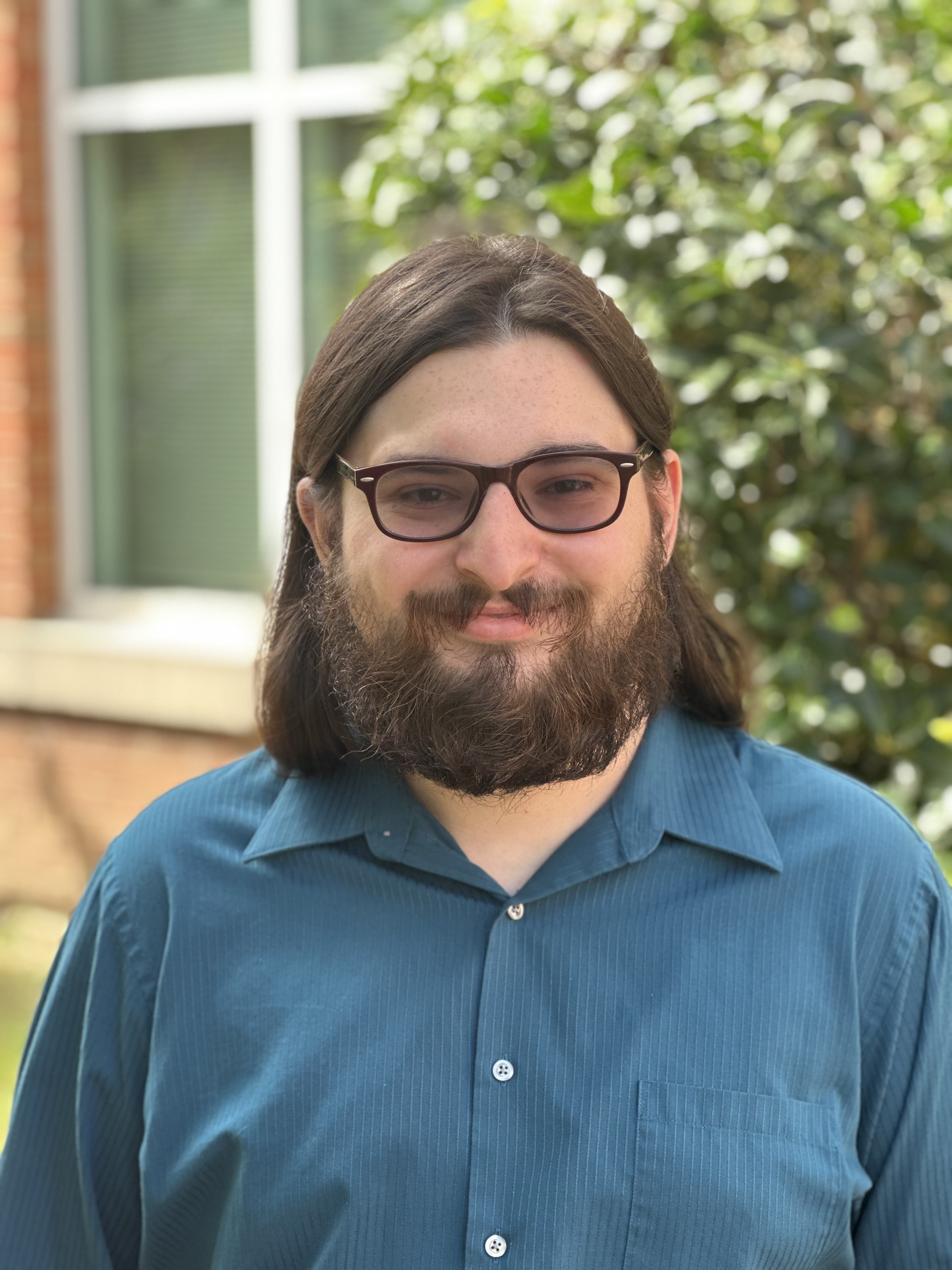 Headshot of Justin Smith, he is smiling. Trees are in the background.